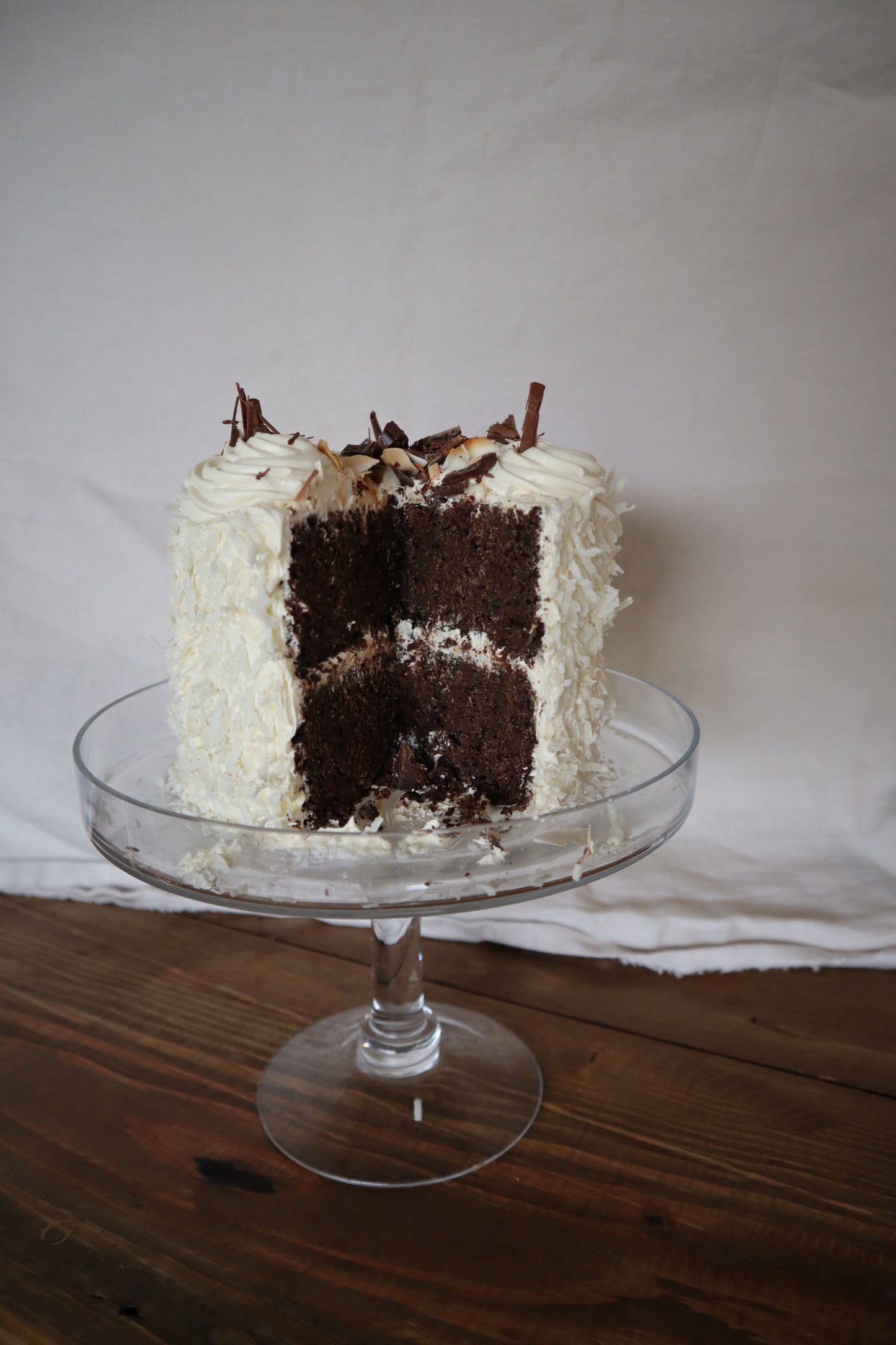 Sourdough-Zucchini chocolate cake with coconut frosting on a glass cake stand against a white background